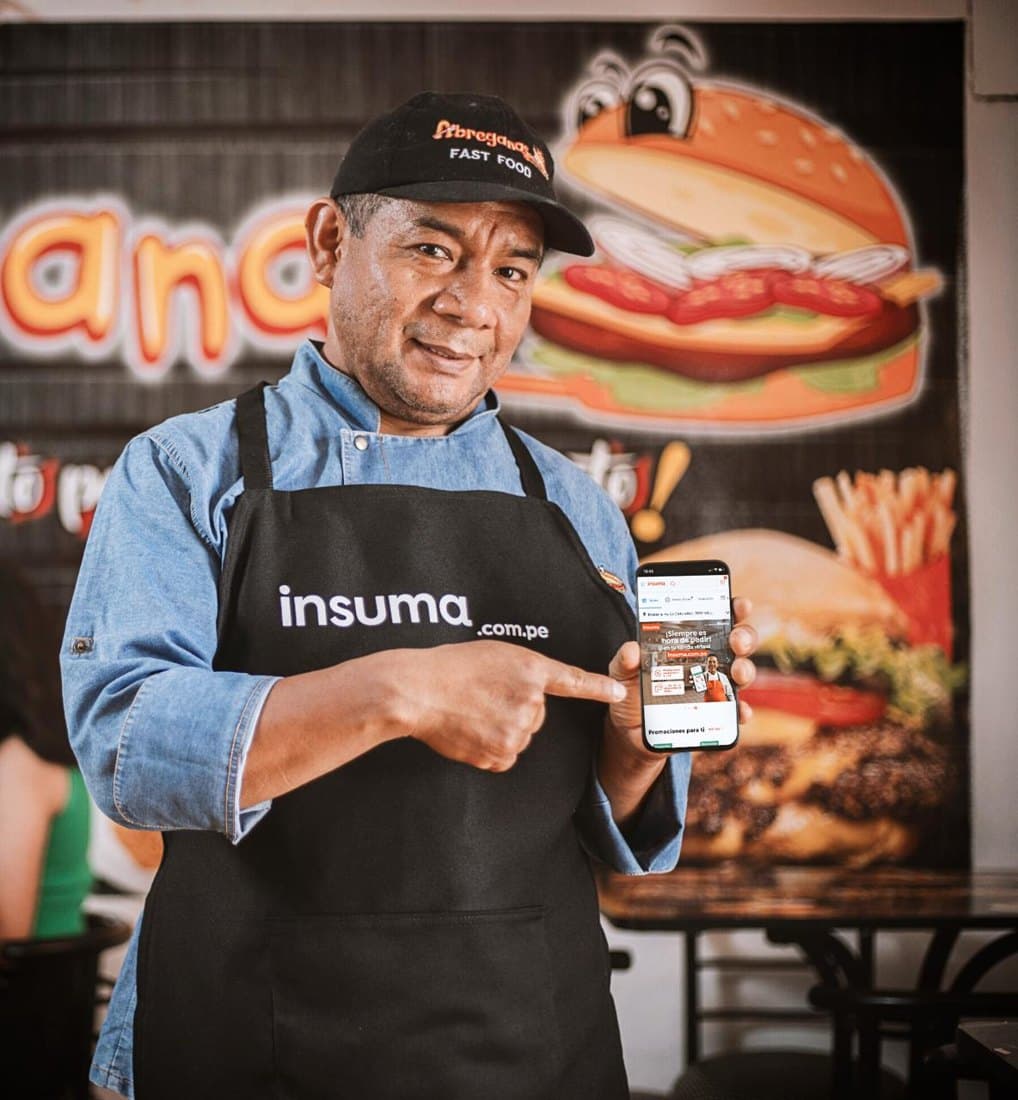 A restaurant owner in an Insuma apron pointing at the Insuma store on his phone